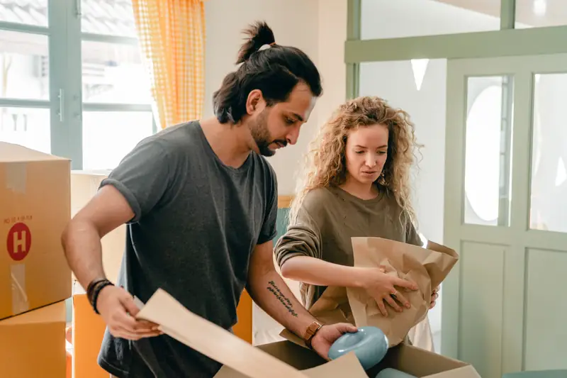 Dues persones emboliquen una peça de vaixella amb paper abans de desar-la en una caixa.